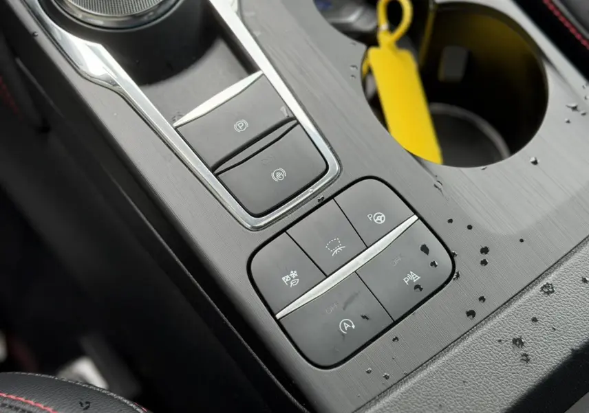 Gros plan sur la console centrale noire avec commandes électroniques et porte-gobelet du Ford Kuga 2023 noir Agathe.