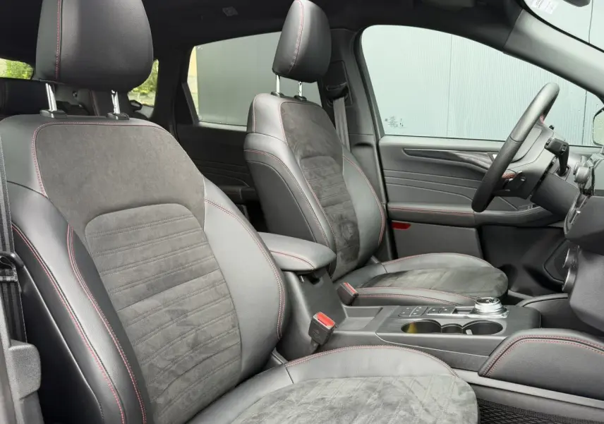 Vue intérieure côté conducteur du Ford Kuga 2023, sièges cuir et alcantara noirs avec surpiqûres rouges et console centrale.