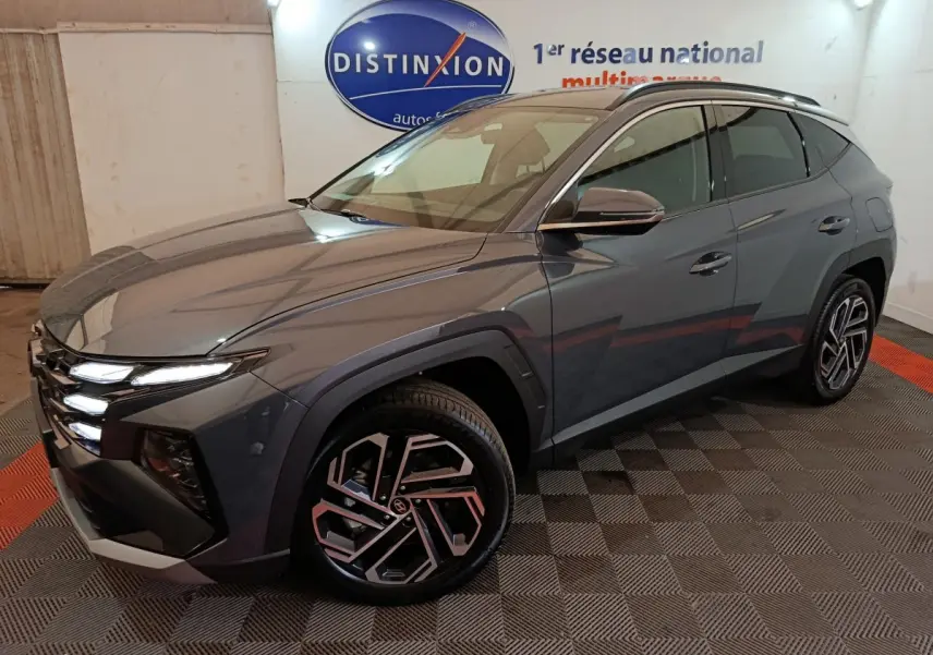 Vue 3/4 avant droit du Hyundai Tucson gris foncé 2025 avec jantes alliage et feux LED allumés en intérieur showroom.