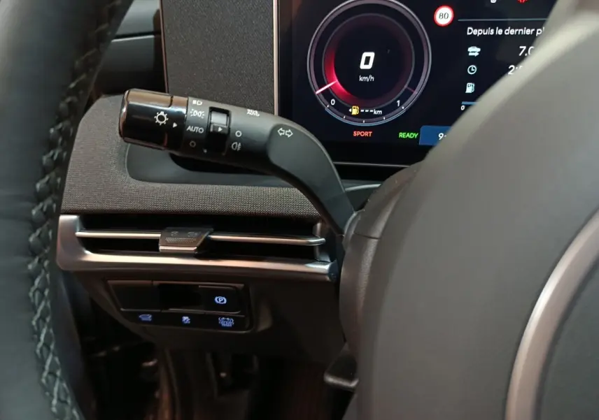 Gros plan sur le combiné d'instruments numérique et la commande des feux à gauche du volant du Hyundai Tucson gris foncé 2025.