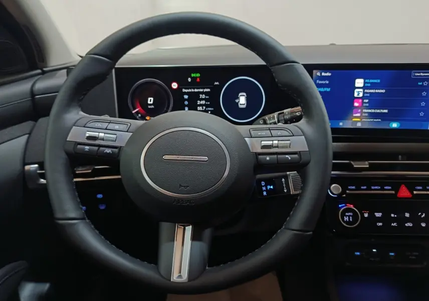 Vue intérieure centrée sur le volant cuir noir et le tableau de bord numérique du Hyundai Tucson 2025 hybride.