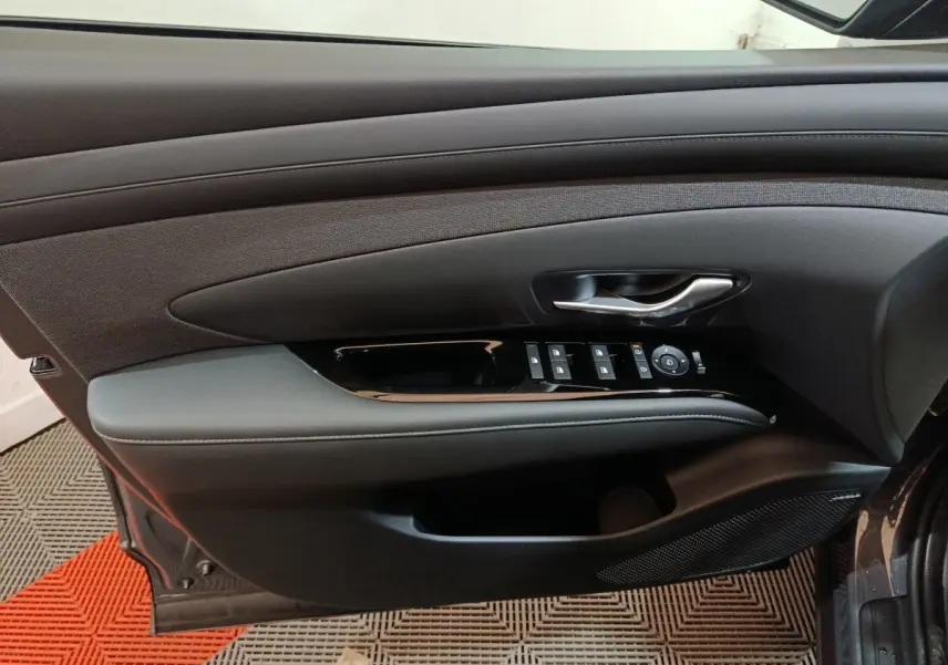 Intérieur côté conducteur de la porte d’un Hyundai Tucson gris foncé, avec commandes électriques et poignée argentée.
