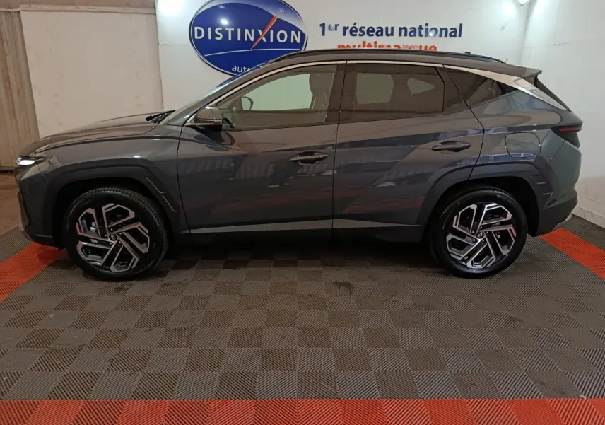 Vue de profil côté gauche d’un Hyundai Tucson gris foncé 2025 avec jantes alliage et toit noir.