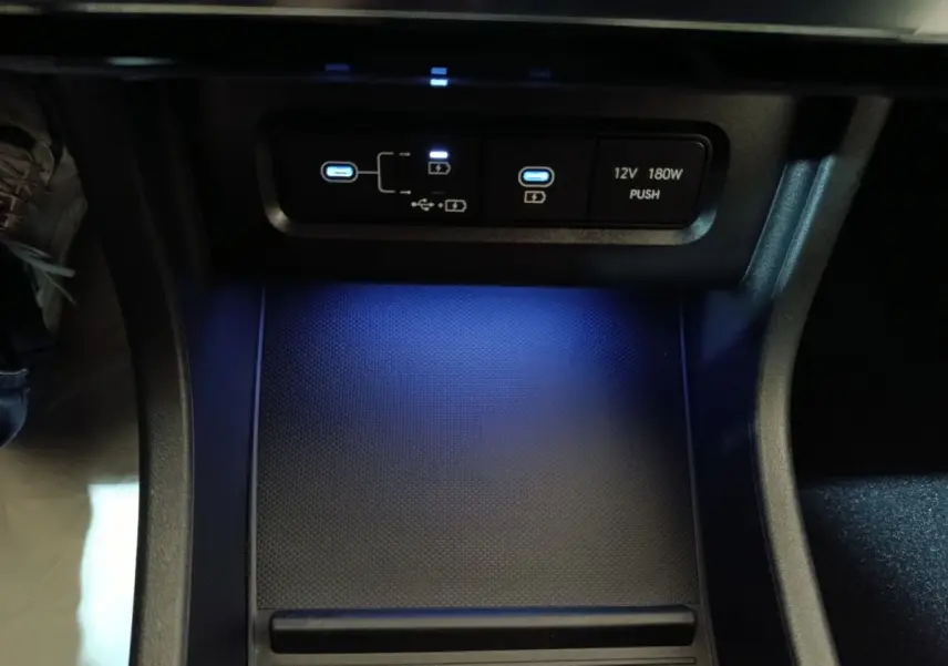 Vue rapprochée de la zone de recharge par induction et ports USB éclairés en bleu dans l'habitacle du Hyundai Tucson gris foncé 2025.