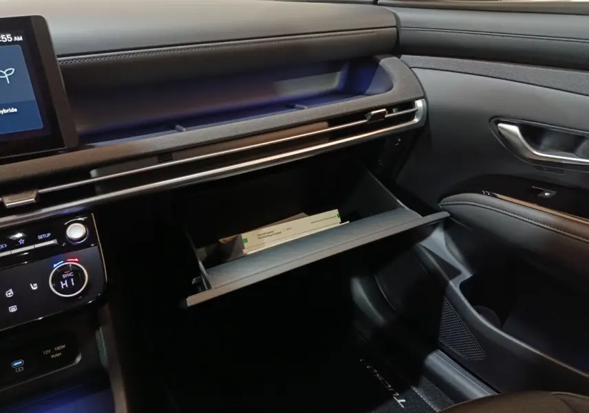 Intérieur du Hyundai Tucson 2025 gris foncé, vue côté passager avec boîte à gants ouverte et tableau de bord moderne.