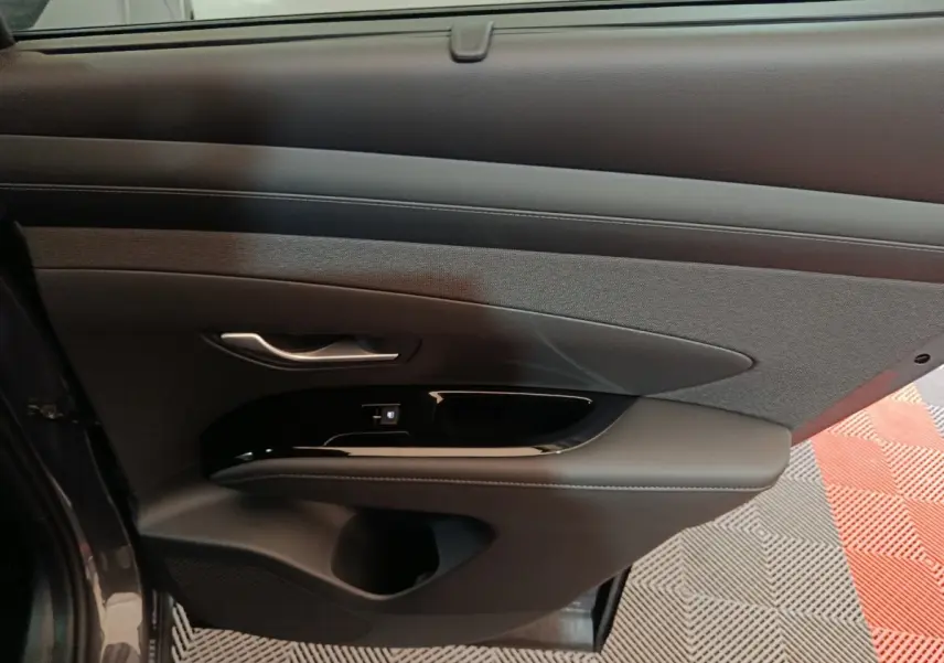 Vue intérieure du panneau de porte avant gauche du Hyundai Tucson 2025 gris foncé, avec commandes électriques et finition tissu et cuir.