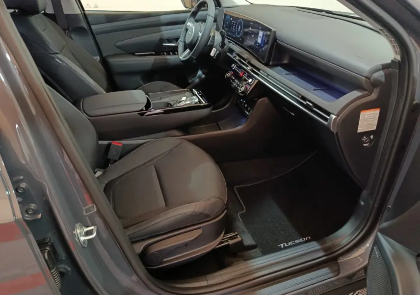 Intérieur avant côté conducteur du Hyundai Tucson gris foncé, avec tableau de bord numérique et sièges noirs.