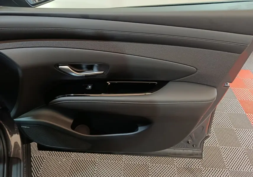 Vue intérieure de la porte avant gauche grise du Hyundai Tucson 1.6 Hybrid 239 Creative avec garniture noire et poignée chrome.