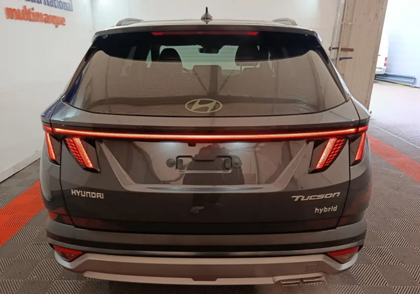 Vue arrière d’un Hyundai Tucson hybride gris foncé avec feux LED allumés et logo Hyundai visible sur le hayon.