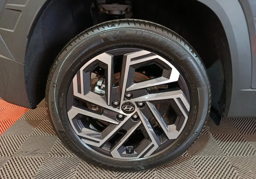 Gros plan sur la jante avant droite du Hyundai Tucson gris foncé, avec design géométrique bicolore et logo Hyundai central.