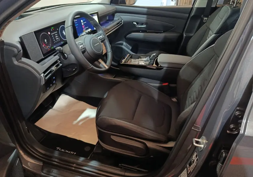 Intérieur avant droit du Hyundai Tucson gris foncé 2025, avec tableau de bord numérique et sièges noirs.