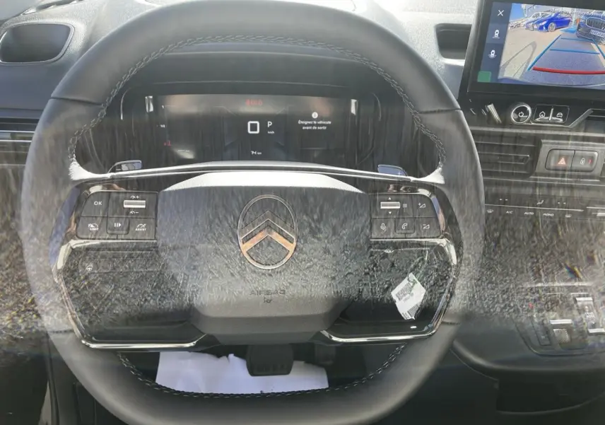 Vue intérieure centrée sur le volant noir du Citroën Berlingo 2026 avec tableau de bord digital et écran de caméra de recul.