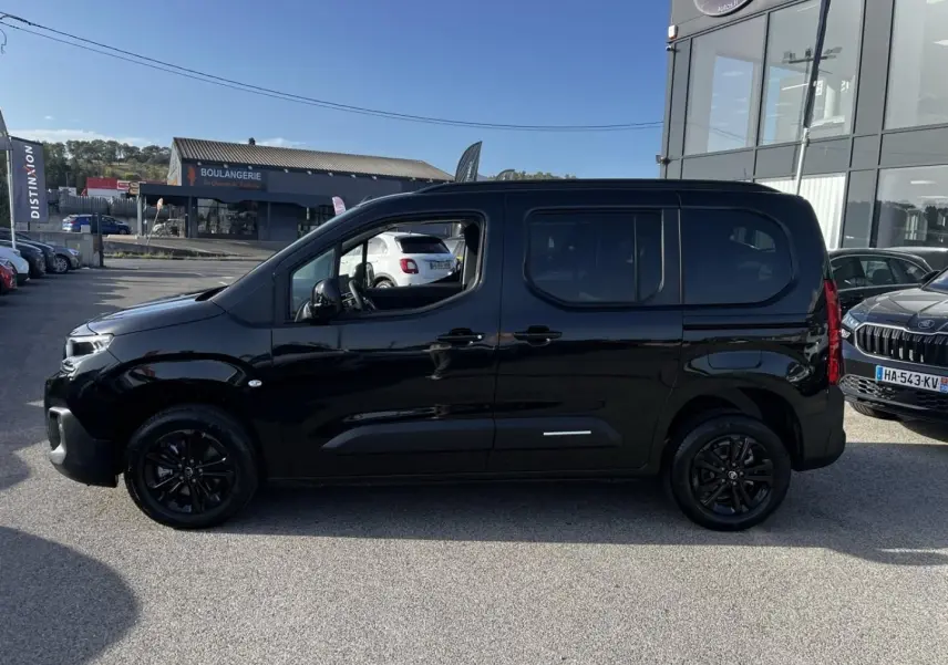 Profil côté gauche d'un Citroën Berlingo noir Perla Nera avec jantes noires, stationné en extérieur au soleil.
