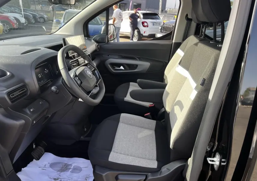 Vue intérieure côté conducteur du Citroën Berlingo noir Perla Nera, montrant les sièges tissu bicolore et le tableau de bord moderne.