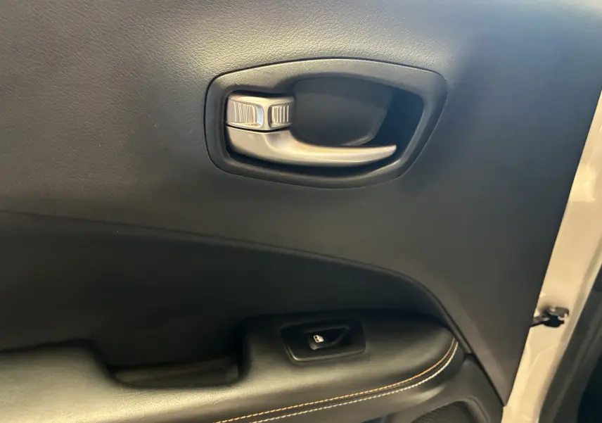 Gros plan sur la poignée intérieure et le bouton de verrouillage de la porte côté gauche du Jeep Compass ivoire.