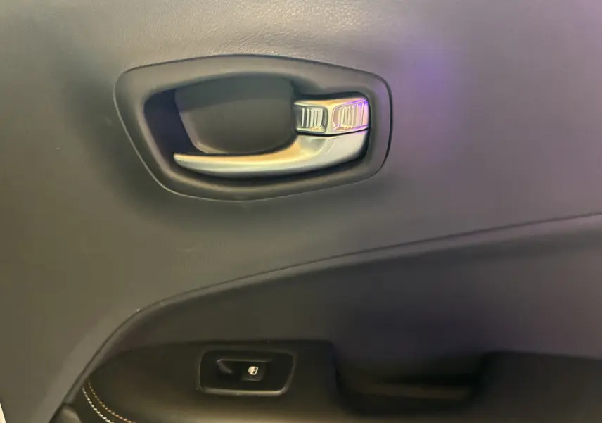 Poignée intérieure de porte côté gauche en plastique noir et métal sur Jeep Compass ivoire, avec bouton de verrouillage.