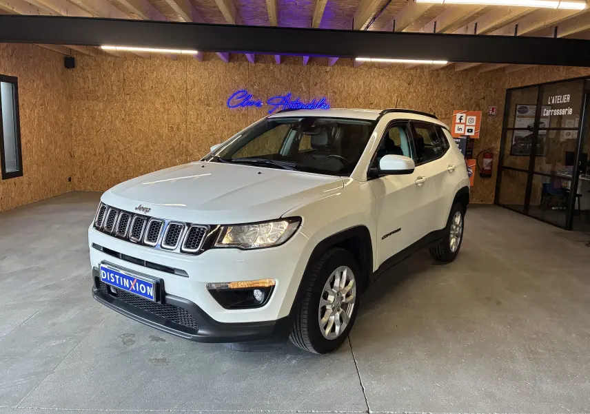 Jeep Compass ivoire en 3/4 avant droit, avec barres de toit et jantes alu, stationné en intérieur sur sol béton.