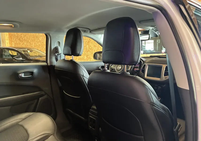 Vue intérieure arrière du Jeep Compass ivoire 2021, montrant sièges avant en cuir noir et tableau de bord avec écran tactile.