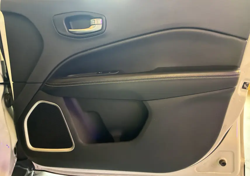 Vue rapprochée de la porte intérieure côté gauche du Jeep Compass ivoire, avec garniture noire et haut-parleur intégré.