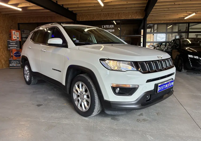 Jeep Compass ivoire en 3/4 avant droit, avec barres de toit et jantes alu visibles en intérieur d'atelier.
