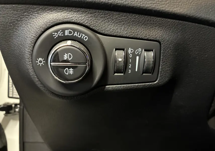 Gros plan sur les commandes d’éclairage noires du tableau de bord du Jeep Compass ivoire, avec réglages automatiques et antibrouillard.