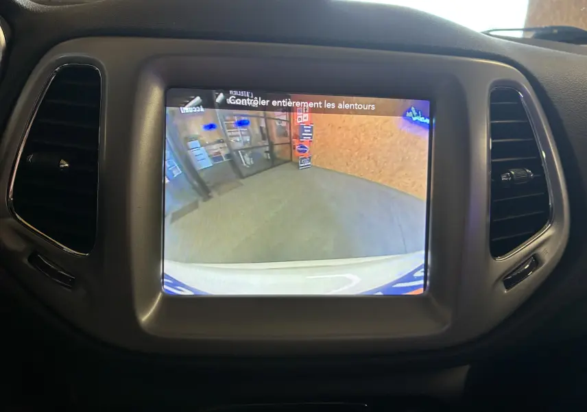 Écran tactile central affichant la caméra de recul dans un Jeep Compass ivoire, vue intérieure du tableau de bord.