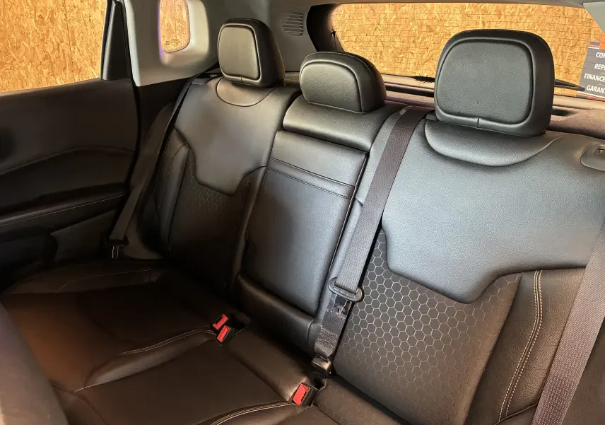Vue intérieure arrière du Jeep Compass 2021, sièges noirs en cuir avec motifs hexagonaux et ceintures de sécurité visibles.