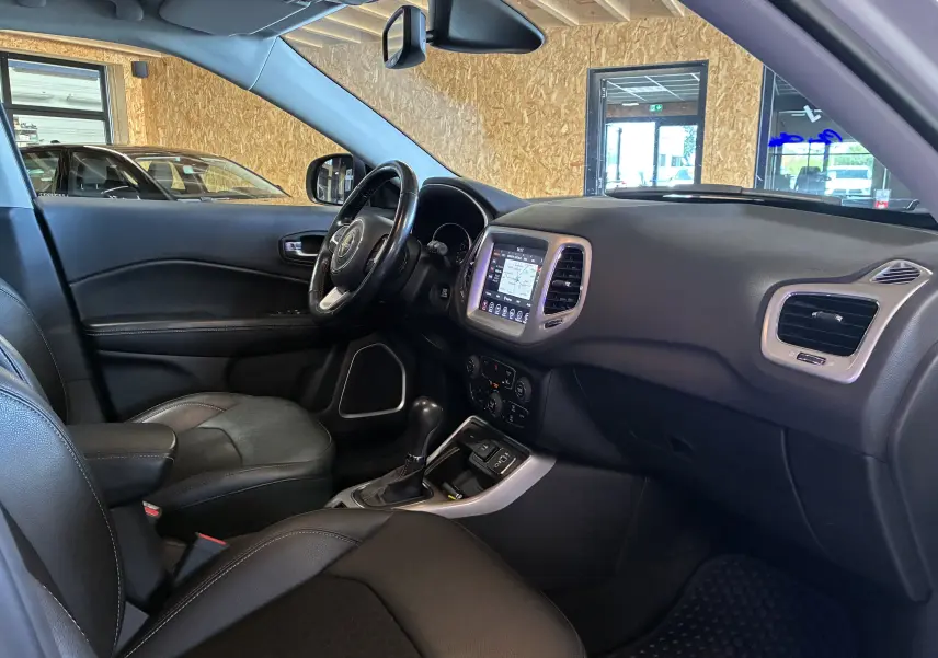 Intérieur noir du Jeep Compass 2021 vu de côté gauche, avec tableau de bord et écran tactile GPS visible.