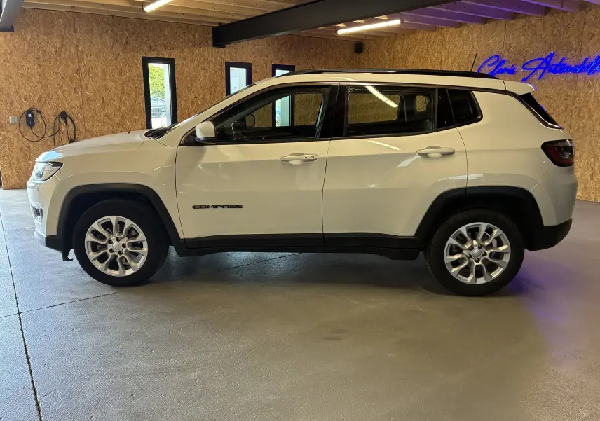 Vue de profil côté gauche d'un Jeep Compass ivoire avec jantes alu et barres de toit, dans un garage intérieur.