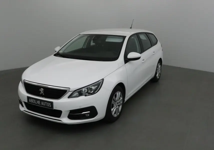 Peugeot 308 SW blanche vue en 3/4 avant droit dans un intérieur neutre avec jantes alliage et calandre noire.