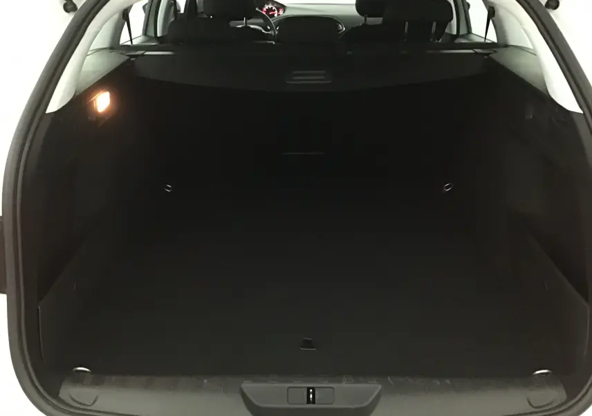 Coffre ouvert d'une Peugeot 308 SW blanche, vue arrière montrant l'espace de chargement vide et l'intérieur sombre.