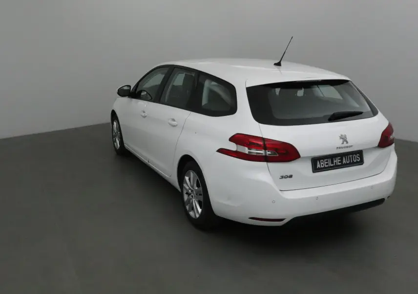 Peugeot 308 SW blanche vue en 3/4 arrière droit, avec feux arrière rouges et antenne de toit visible.
