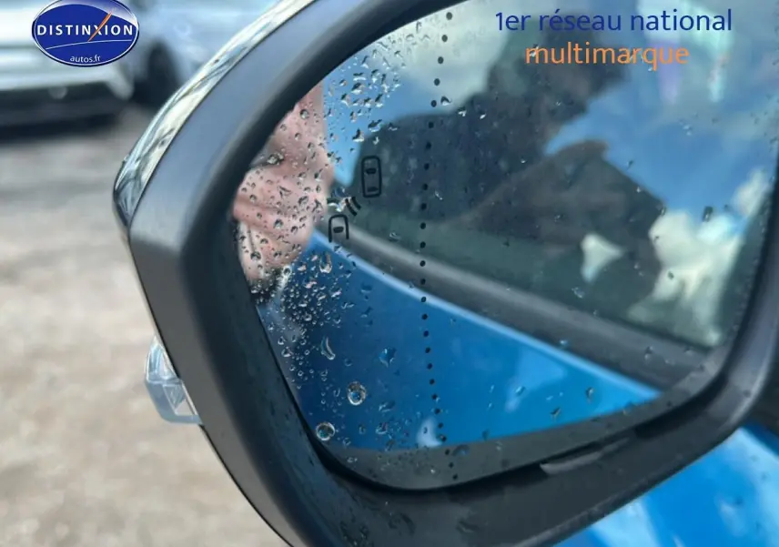 Rétroviseur droit de Renault Austral bleu 2026 avec gouttes d'eau et indicateur d'angle mort visible.
