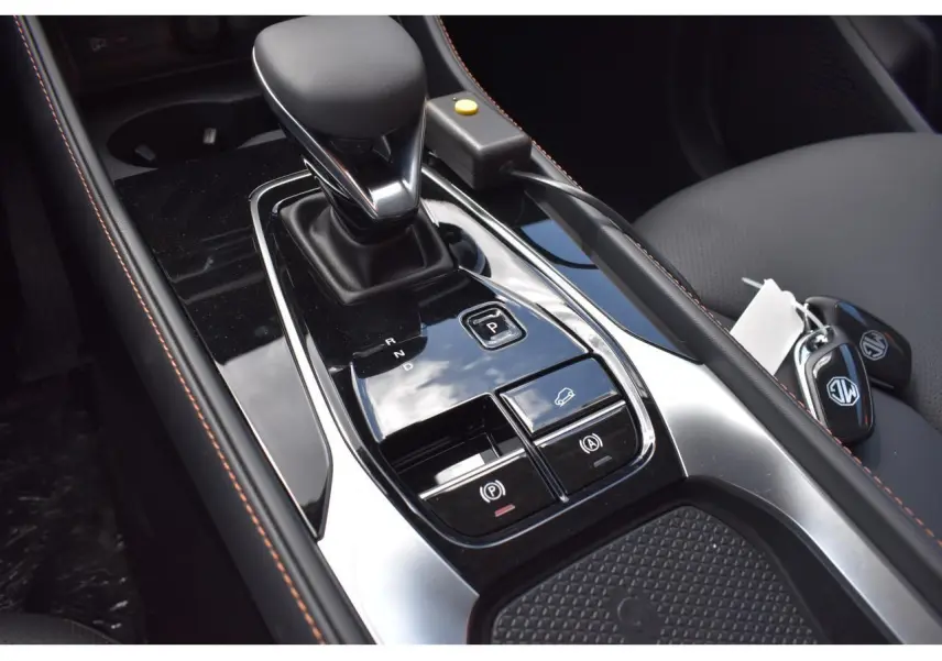 Gros plan sur la console centrale noire brillante du MG Motor EHS gris, avec levier de vitesse automatique et clés visibles.