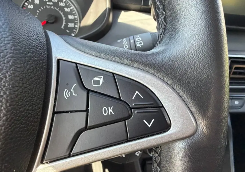Gros plan sur les commandes au volant noir et argenté du DACIA Sandero 2025, avec tableau de bord partiellement visible.