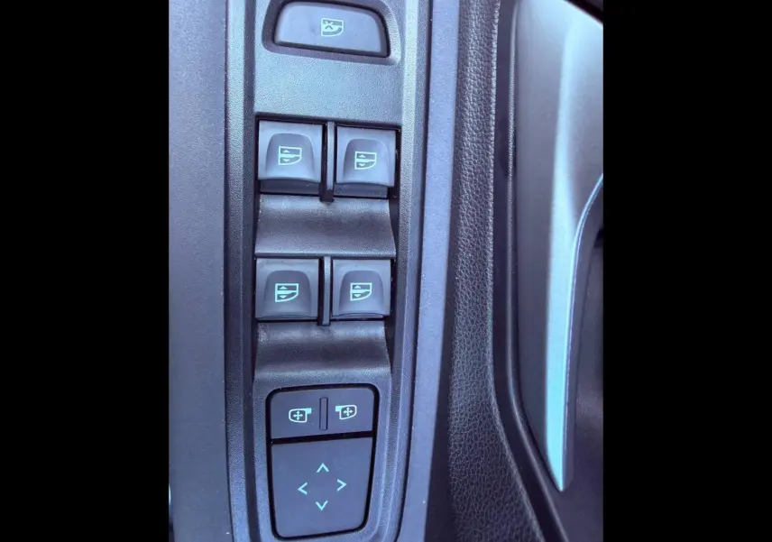 Gros plan sur les commandes des vitres électriques et réglages des rétroviseurs côté conducteur de la Dacia Sandero kaki.