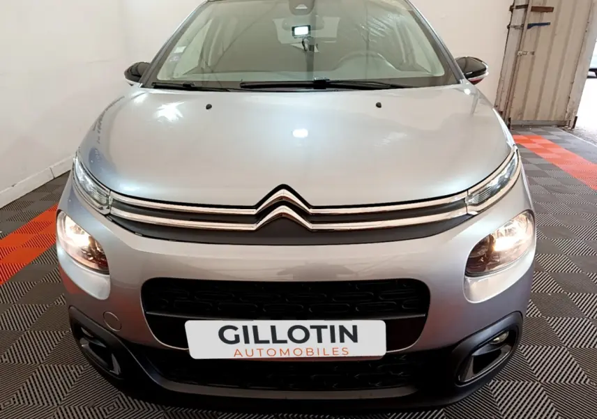 Vue avant d'une Citroën C3 gris clair de 2019 avec phares allumés et logo distinctif sur calandre chromée.