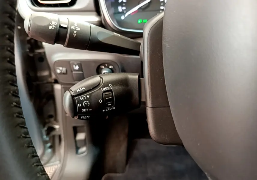 Gros plan sur la commande de régulateur de vitesse à gauche du volant cuir d'une Citroën C3 gris clair 2019.