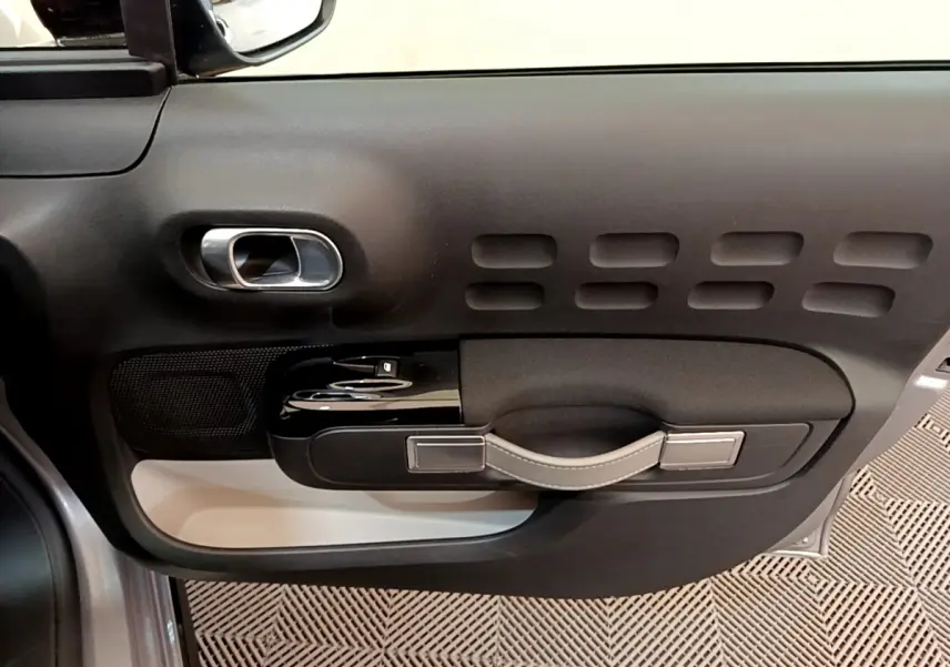 Vue rapprochée de la porte côté gauche intérieure de la Citroën C3 gris clair avec poignée en cuir et commandes électriques.