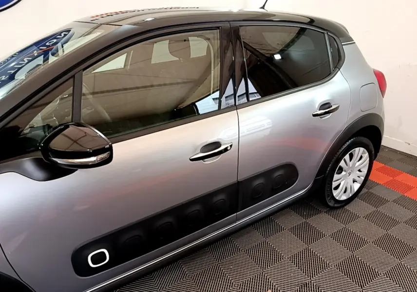 Vue latérale côté gauche d'une Citroën C3 gris clair avec protections noires caractéristiques sur les portières.