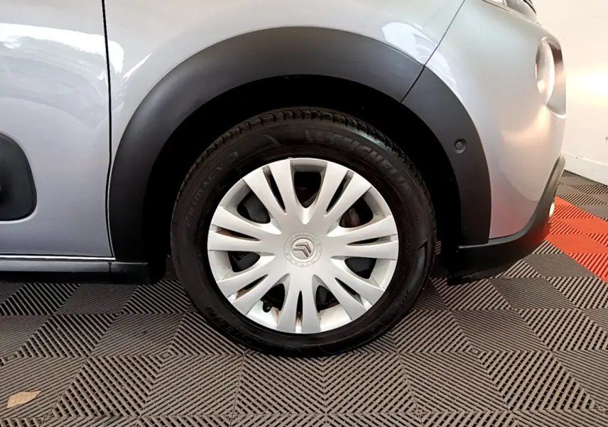 Gros plan sur la roue avant droite d'une Citroën C3 gris clair, avec jante en acier et enjoliveur blanc.