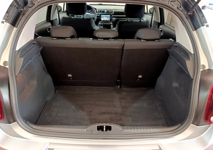 Coffre ouvert d'une Citroën C3 gris clair vue de l'arrière, montrant l'habitacle et l'écran tactile du tableau de bord.