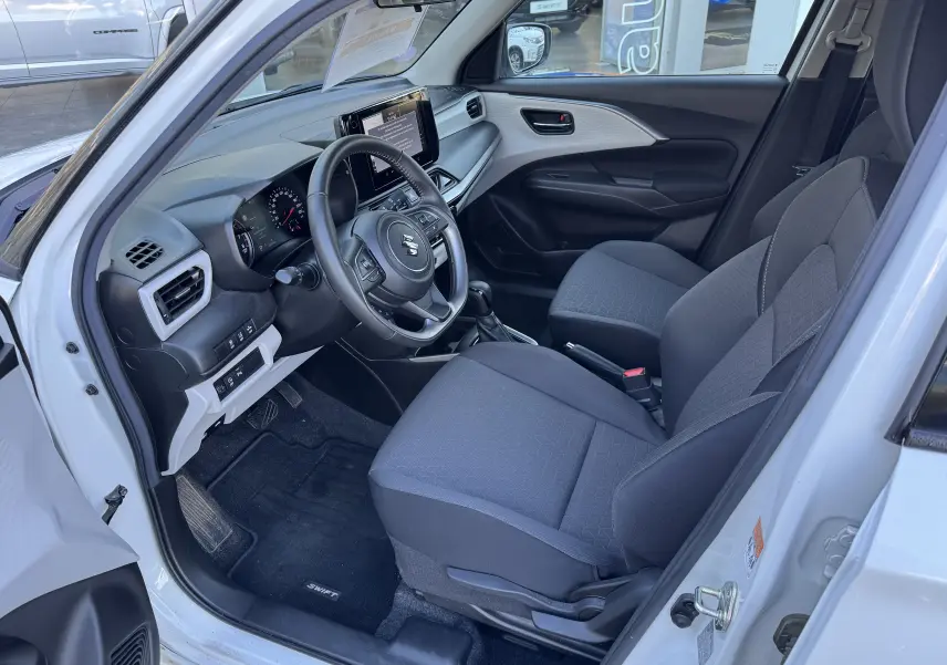 Vue intérieure côté conducteur de la Suzuki Swift 1.2 Dualjet Pack Auto Hybrid 2024, sièges gris et tableau de bord moderne.