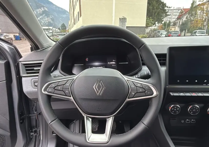 Vue intérieure centrée sur le volant cuir multifonctions d’une Renault Clio gris schiste, tableau de bord et écran tactile visibles.