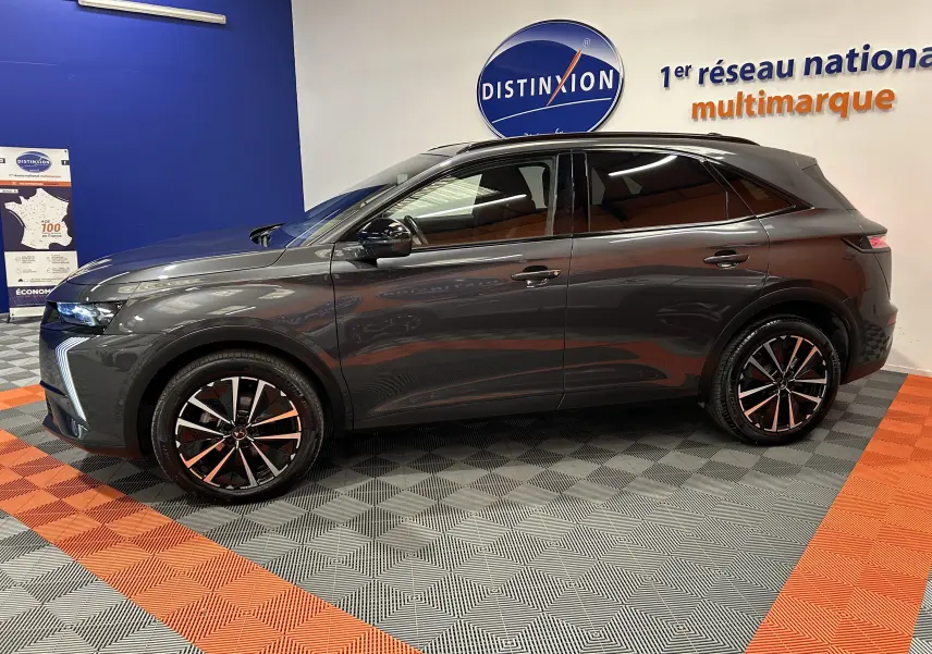 Vue de profil côté gauche du SUV DS7 BlueHDi 130 gris titane avec jantes bi-ton et hayon électrique en intérieur showroom.