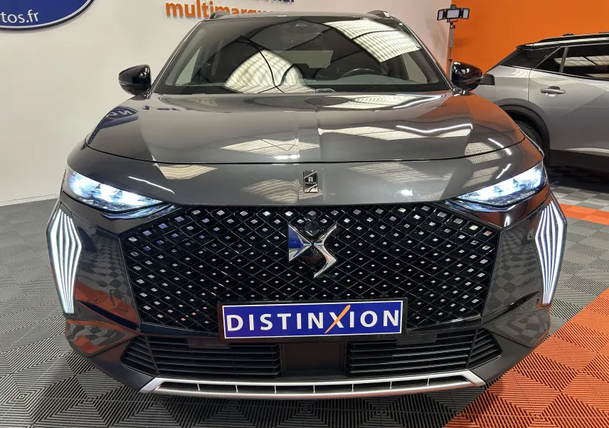 Vue avant d'un DS7 gris titane avec calandre noire à motif losange et feux LED allumés en intérieur showroom.