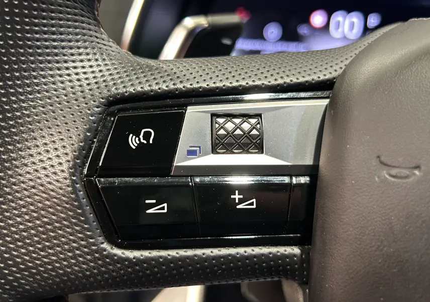 Gros plan sur les commandes multifonctions noires et argent du volant perforé du DS7 gris titane, version 2024.