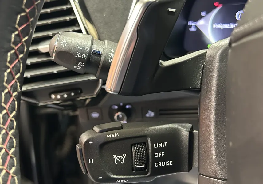 Gros plan sur la commande de régulateur de vitesse au volant d’un DS7 2024, intérieur noir avec surpiqûres rouges.