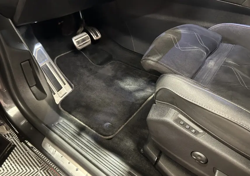 Gros plan sur le pédalier et le siège conducteur en cuir noir avec surpiqûres, intérieur du DS7 gris titane.