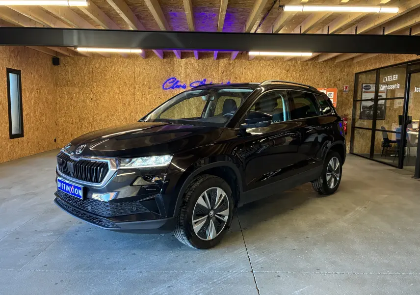 Vue 3/4 avant droite d’un Skoda Karoq noir 2024 avec calandre noire chromée et jantes alliage 17 pouces dans un garage.